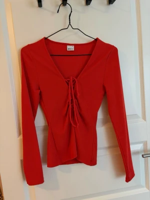 Orange ribbad topp med snörning - Djup v-ringning och toppen är figurnära i modellen. Mer åt orange hållet i verkligheten. Sitter mer som i storlek S än M. Använd en gång 