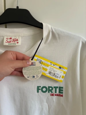 Vit t-shirt Saint Barth Forte dei Marmi - Vit t-shirt från Saint Barth i ekologisk bomull med trycket 'FORTE DEI MARMI' i grönt och rött på bröstet. Klassisk passform med rund halsringning och korta ärmar. Liten logga även på ärmen. Perfekt för en chill och stilren look.