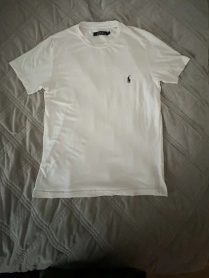 Vit t-shirt från Polo Ralph Lauren - Klassisk vit t-shirt från Polo Ralph Lauren med liten broderad logga på bröstet. T-shirten har rund halsringning och korta ärmar. Tillverkad i mjuk bomull för en skön och avslappnad känsla.