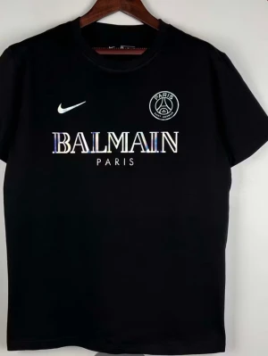 Svart Balmain x PSG t-shirt - Snygg svart t-shirt med Balmain Paris-tryck och PSG-logga på bröstet. Klassisk Nike swoosh på ena sidan. T-shirten har rund hals och korta ärmar, perfekt för dig som gillar streetwear och sportig stil.
