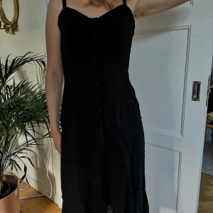 Svart sommarklänning - Fin svart sommarklänning med knappar och snygg öppning i ryggen. Perfekt till vardags eller till stranden. Modell 173 cm. Köpen står för frakt. 