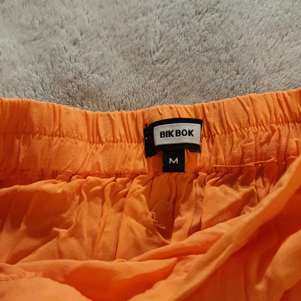 Orange kjol med resår i bak för bättre passform. Lite tunnare vilket gör att svarta underkläder lyser igenom på mig, vitt fungerar bra! Även hotpants (korta cykelbyxor) fungerar bra. M, men passar även S. Kjolar.