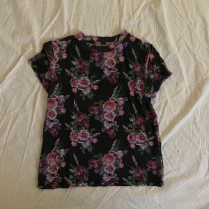 Blommig t-shirt  - Mörk t-shirt med blommigt mönster. Tröjan kommer från Carlings och märket /STAY. Storleken säger XS men skulle säga att det i alla fall är en S. 