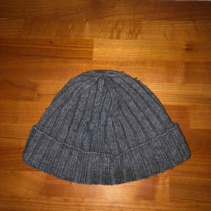  - Mörkgrå mössa från J.Lindeberg. Lite nopprig. 