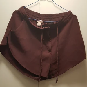  - Rundade shorts i vinrött, tunnt och svalt tyg. Fickor och blixtlås framtill. Även knytband för att justera storleken. Lite högre i midjan men kortare i benen, kan därmed också funka för något större än strl M.