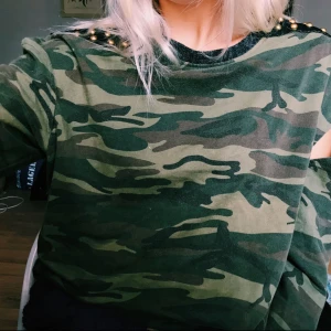  - Tröja med nitar på axlarna. Som ni ser på bilden så är lappen sönder men det är endast det som är paj. På båda axlarna så ser man att det är öppningar på både framsidan och på ryggen. (Kolla bilderna)