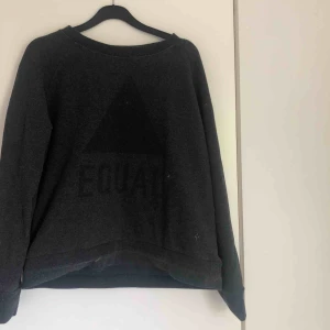  - Tröja från Lager 157. Svart triangel med texten ”EQUAL” på framsidan, syns knappt
