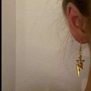 Örhängen, smycken - I04. Jättefina örhängen i guld med stjärnor och blixtrar på. Glöm inte att 10% av vinsten går oavkortat till organisationen kvinna till kvinna. 