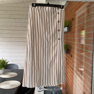 Kjol - Vit och beige randig kjol med bruna knappar samt en liten slits. Oanvänd & lappen är kvar. Storleken är 38 men funkar är även som 36. Frakten är inräknad i priset.