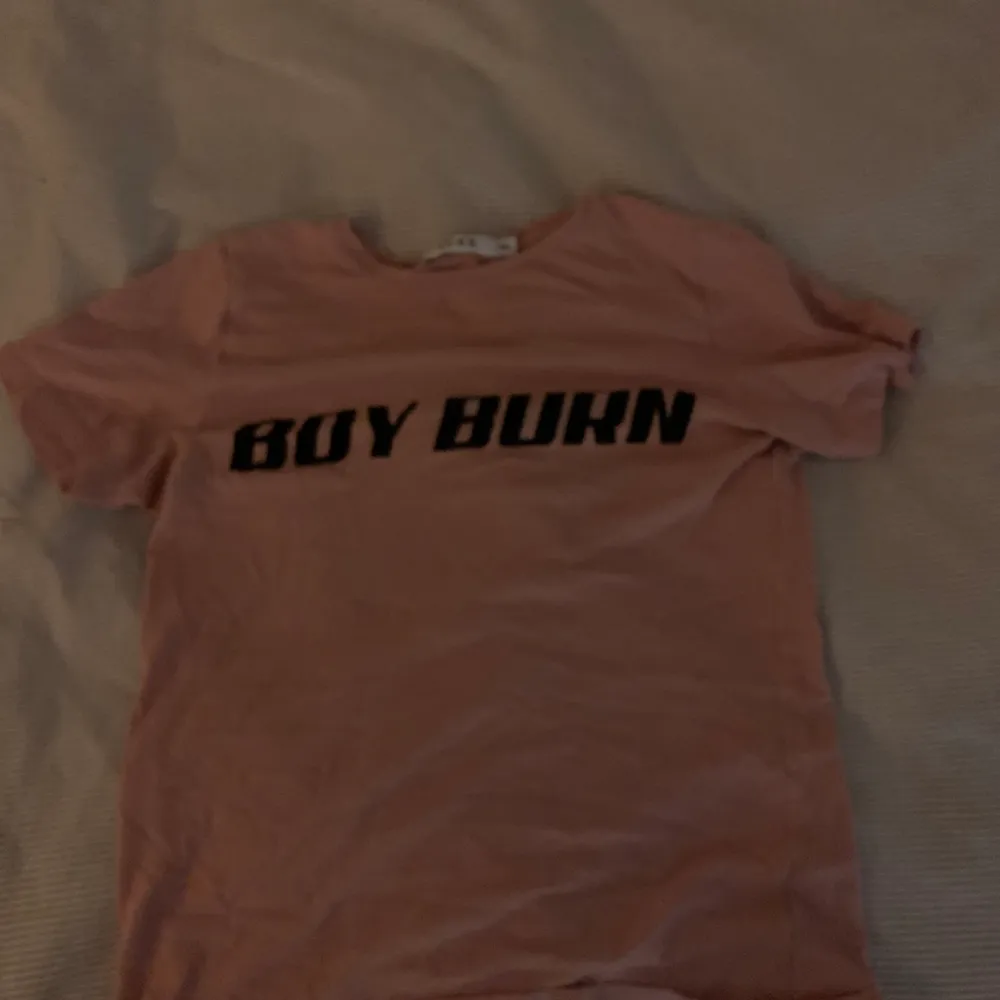 T-shirt från na-kd med text: boy burn, rosa i färgen, blir enkelt skrynklig säljer den därför för ett billigt pris. Säljer den för att den är för liten . T-shirts.