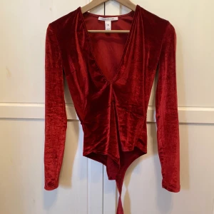 Röd festbody - Röd långärmad festbody med djup urringning i sammetsliknande material. Använd 1 gång i väldigt bra skick. Köpt från Nelly.com.  Kampanj: KÖP 3 BETALA FÖR 2
