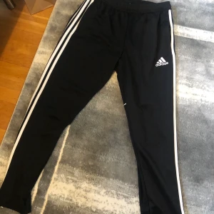 Adidas byxor - Ett par adidas byxor svarta med vita ränder vid sidan av byxan. Plagget är använd minst 3 gånger och är i väldigt bra skick. Funkar jätte bra till  träning och ha som vardags.
