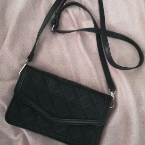 väska  - Smidig och fin axelremväska som även går att använda som kuvertväska eftersom remmen är löstagbar. I svart mjukt konstläder. .