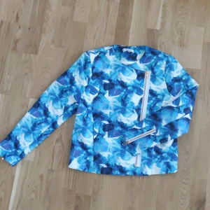 Tunn jacka AngelicaBlickxBikbok kollektionen stl M - En tunn croppad jacka från AngelicaBlickxBikbok kollektionen. Blå och vit mönstrad med rosefärgade dragkedjedetaler i mitten på jackan och i slutet på ärmarna. Har "osynliga" fickor på framsidan. Fraktkostnaden tillkommer.