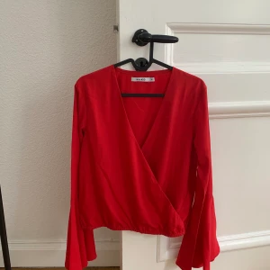 Omlott-Blus - Röd omlott-blus med vida armar stl: 36 från NAKD. Enbart använd vid ett fåtal tillfällen så mycket bra skick. Finns att hämta vid Östermalmstorg eller skickas mot avgift. 