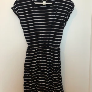 Sommarklänning  - En härlig randig sommarklänning i marinblå och vit. Fickor på framsidan och resor i midjan. Klänningen är i fint skick och bara använd ett fåtal gånger. Köparen står för frakten.