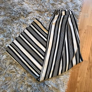  - Vida svartvitrandiga byxor i skönt, tunt tyg. Köpta här på plick, men aldrig använda av mig. Den tidigare ägaren har dock gjort två små fläckar, en i grenen (så den syns inte när plagget är på) och en liten längst ner på baksidan av ena benet (se bild). Fraktkostnad tillkommer!