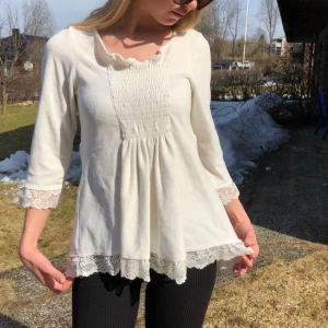  - Vit blus i plysch med spets i ärmslutet och längst ned på tröjan. Ribbad över bröstet och lite längre baktill. Superfin! 