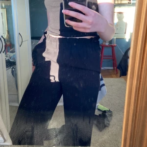 Svarta kostymbyxor - Ett par svarta kostymbyxor, de sitter inte tight utan är mer flowiga!! Väldigt sköna, använda några gånger men har inte använts på ett tag nu därav försöker jag hitta någon som kommer älska de lika mycket som jag har gjort!!! Jag är 173cm och de går precis ner till marken! Midjan är lite hög plus detaljer vid midjan! 