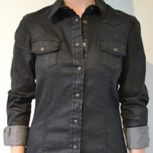  - Svart jeansskjorta med ytbehandling som gör att den får ett läderliknande utseende. 