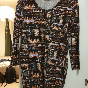 Mönstrad klänning - Långärmad klänning, urringad i ryggen. Oklar storlek men sitter lite loose fit på mig som brukar ha 36.