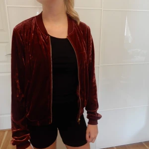 Munkjacka i sammetliknande material - Munkjacka i mörkrött sammetliknande material med guldig dragkedja. Storlek XS. Fungerar även för S. 