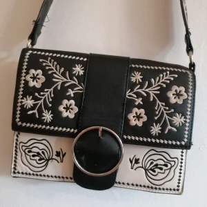 Väska från Stradivarius - Väska med fin blombrodyr från Stradivarius. Har använt den mycket, därav lite sliten men annars superfin! Har en fläck på framsidan (se bild 3) men ingenting man tänker på tycker jag 😊 50 kr + frakt 🌼 Kan även hämtas/ mötas upp i Gbg! 