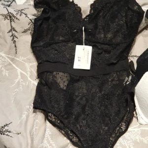 Svart body  - Säljer oanvänd body med spets. Genomskinlig och resårband i midjan. Köparen står för frakten. Bud startar från 50kr och måste höjas med 50kr
