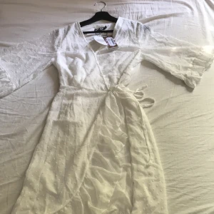 Omlottklänning från boohoo, helt oanvänd - Vit omlottklänning från boohoo i skönt flowy material i storlek 38. Helt oanvänd, den passade inte mig. Kan vara tajt över bysten om du har en lite större byst. 250kr + frakt