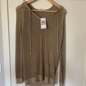 Michael Kors knitted hoodie - Detta är en tunn stickad hoodie från Michael Kors med v-rigning. Tröjan är oanvänd och prislapp finns kvar. Tröjan är gjord av 82% rayon och 12% polyester samt även 6% guldmetalltråd. Tröjan passae fint med såväl klänning som jeans och passar en storlek S för en slimfit, men även mindre storlekar för en mer loose fit. Tröjan är som tidigare nämnt oanvänd och i mycket bra skick. Pris kan diskuteras.