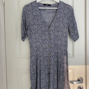 Blommig klänning - Blå blommig klänning med ljusa blommor och knappar framtill ifrån Bikbok stl S.