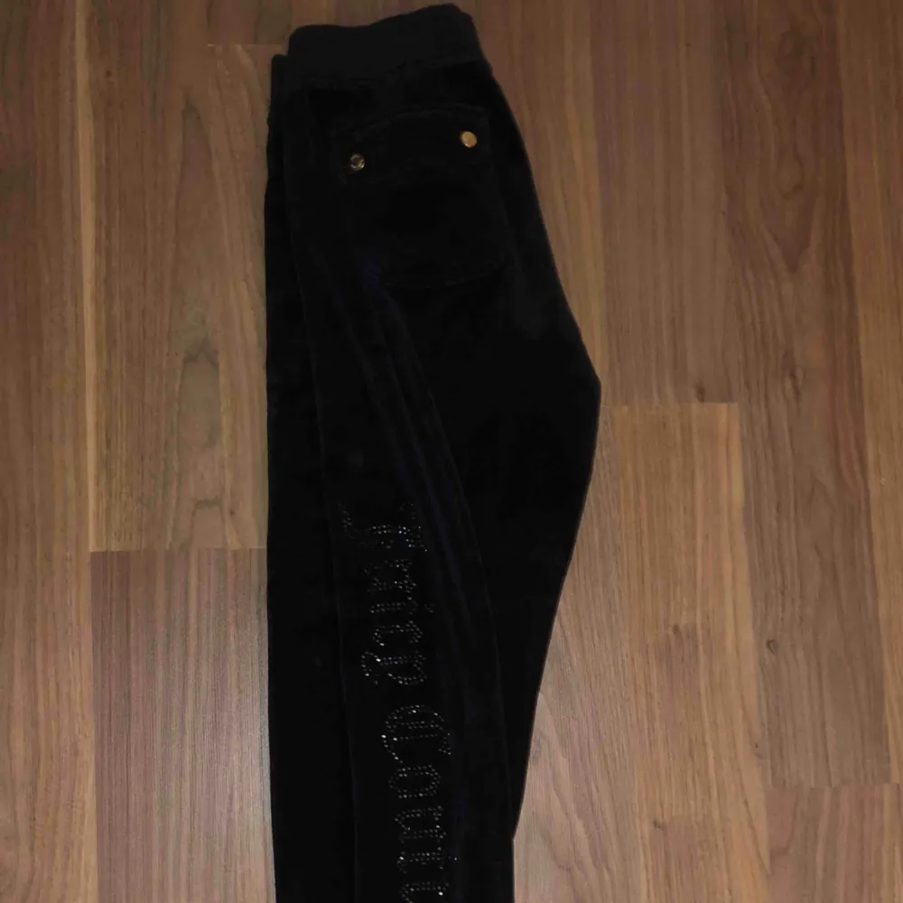 Svarta mjukisbyxor från juicy couture med svart glittrig text längst benet. Jeans & Byxor.
