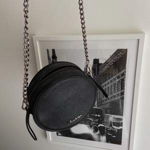 Aldrig använd i nyskick, en svart puck formad väska med svart lyster. Med ett Cross body band, Nypris 650kr 