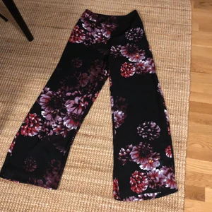 Vida byxor - Härliga vida byxor i svart med röda/lila blommor. Höga i midjan och luftigt material😍 Från Lindex och aldrig använda. Strl 36. Mottagaren betalar frakten😊