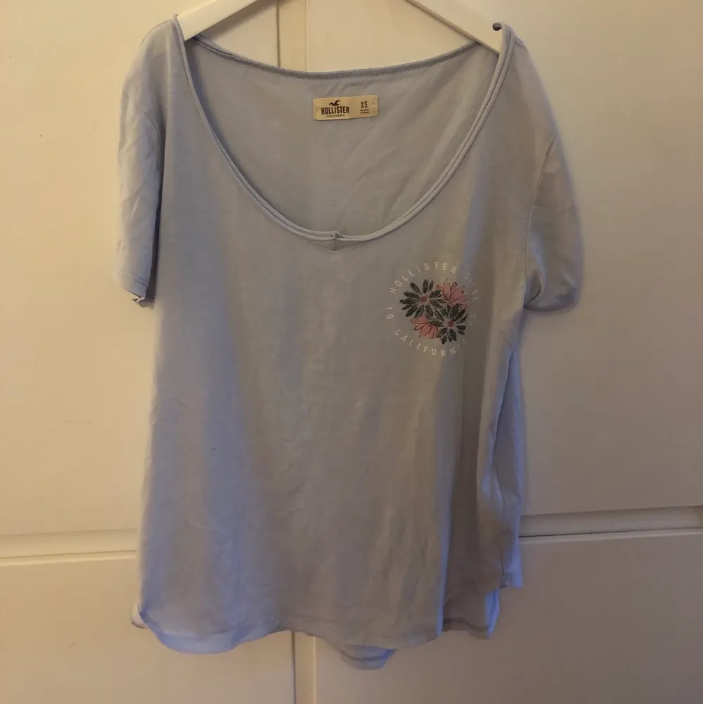 Jättesnygg ljusblå t-shirt med blommor över högra bröstet, där det runtom står hollister. Köpt för 180 kr, säljer för 40 kr.. T-shirts.