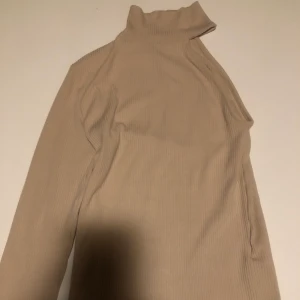 Ribbad enärmad tröja - Nude färgad. Använd en gång! Enkel polokrage. Väldigt snygg på och väldigt snygg till jeans. FRAKT TILLKOMMER.