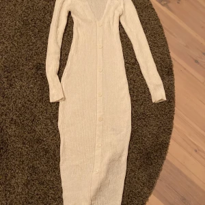 Lång stickad klänning  - Lång stickad klänning med knappar fram. Slutar en bit ovanför anklarna. Slits på båda sidor. Lite genomskinlig men inget som märks om du inte har neon färger på underkläderna. 