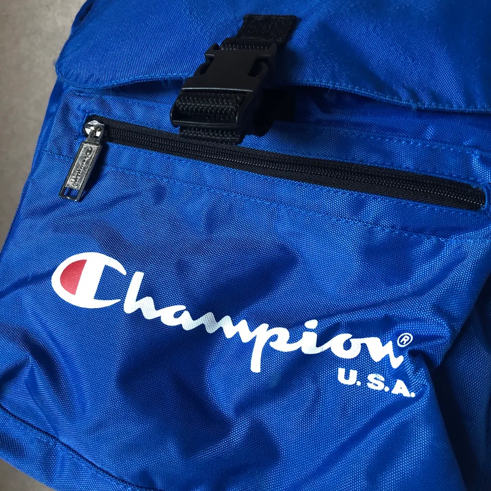 Kornblå ryggsäck från Champion. Rymlig med många fack. Resår i öppningen.. Väskor.