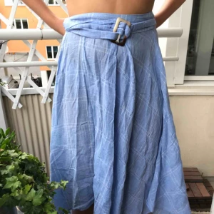  - Ljusblå kjol med vita tunna rutor (se bild). Skärp till i midjan vilket gör att både en medium person och en XL person kan passa i kjolen. (Köper står för frakten)