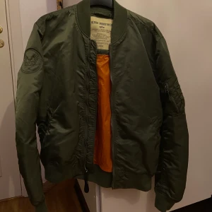 Alpha Industries Jacka - Säljer min brors gröna bomberjacka som är från Alpha Industries. Tyvärr är den röda flärpen som brukar sitta på armen borta. Storlek Large men den passar ändå mig som annars brukar vara S bra- men jag gillar ju oversized så kan va därför. Unisex men är köpt från herravdelningen. Den är ej använd, han köpte den endast och orkade inte lämna tillbaka den då den inte satt bra på honom. Blir det många intressen så blir det bud. Frakt betalas av köpare. Snabb affär om du kommer med rimligt pris. Nypris: ca 1500kr 