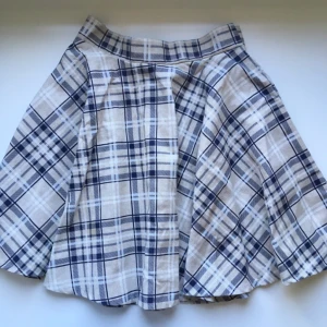  - Rutig cirkelkjol i blå,vit och beige. Midja 65cm. Har själv sytt den, därav det slarviga och sneda blixtlåset på baksidan.  Styvt tyg, så den står ut fint från midjan.