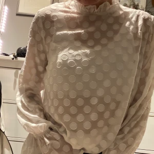 Vitprickig blus - Säljer denna sjukt söta blus från NA-KD, den är i ett genomskinligare tyg med vita prickar. Knytningar vid ärmen samt hög krage. Sitter sjukt fint och faller så najs på kroppen! Köpare står för frakt ❤️❤️