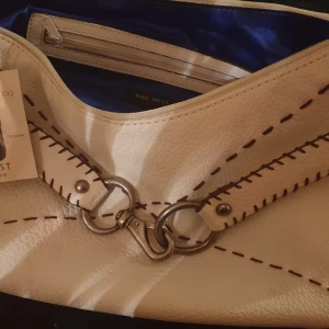 Väska Nine West  - Helt oanvänd vit väska med bruna insydda inslag och fransar. Ingår liten söt matchande väska. Innerfoder mörkblå sidenkänsla
