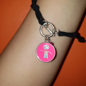 Armband - Armband med smycke, köpt från en välgörenhet men kommer ej ihåg vilken. Armbandet är något mockaliknande material.