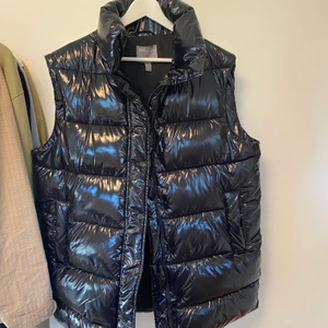 Svart glansig dunväst - Intressekoll på denna väst! Skitsnygg väst som går över rumpan i oversized stil. Storlek 38 köpt på asos i bra kvalitet. 