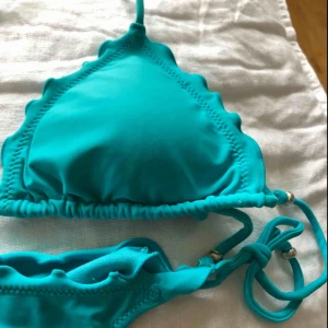  - Ljusblått bikiniset från Wonderland, Nelly, i storlek M. Ruffle trekantsbikini-BH, schrunch på baksidan av bikiniunderdelen. Båda i storlek M/US 6/EUR 12-14. Nyskick! En silverfärgad kula i varje band, en saknas i snöret bak på ryggen i bikiniöverdelen.
