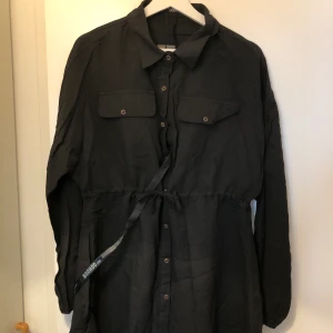 Svart skjortklänning - Svart skjortklänning med resår i midjan. Aldrig använda, lapp kvar. För kort för mig som är 177cm.