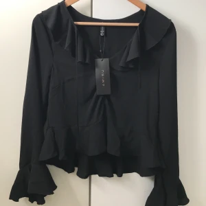 Svart blus - Svart blus med lappen kvar från New Yorker. Fina detaljer med volanger och knappar. Frakt tillkommer