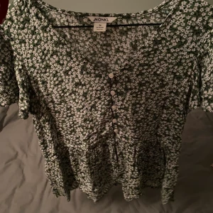 blus blommor grön  - Grönvit blus från Monki med små blommor på. Extremt fin och skön på sommaren. Har en liten mini ”kjol” på. Storlek 36 som passar mig som är S/M. Originalpris 350 kr