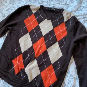 Brun stickad tröja - Brun stickad tröja med argyle mönster. Brun och mönster i orange och vitt. Bra skick. Storlek XL.